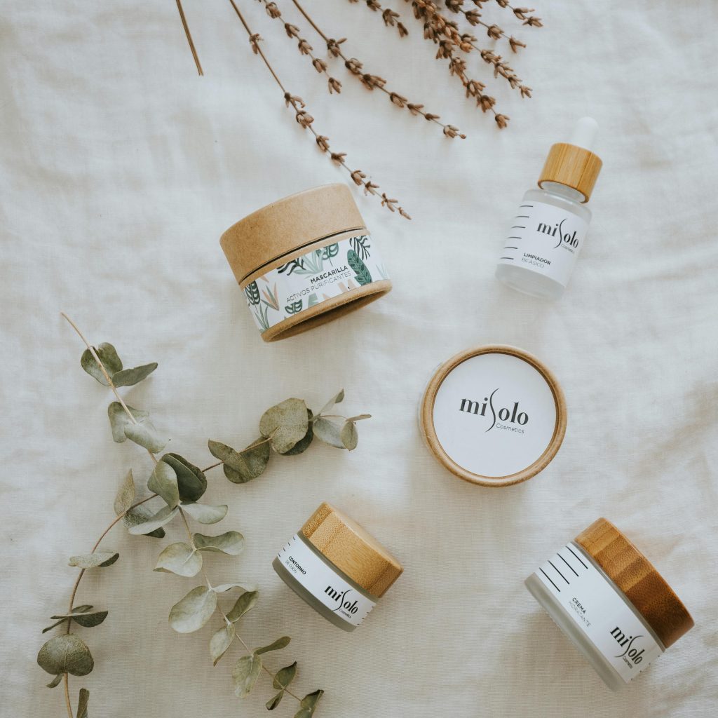 Minimalistic flatlay of eco-friendly beauty products with botanical elements on white fabric.